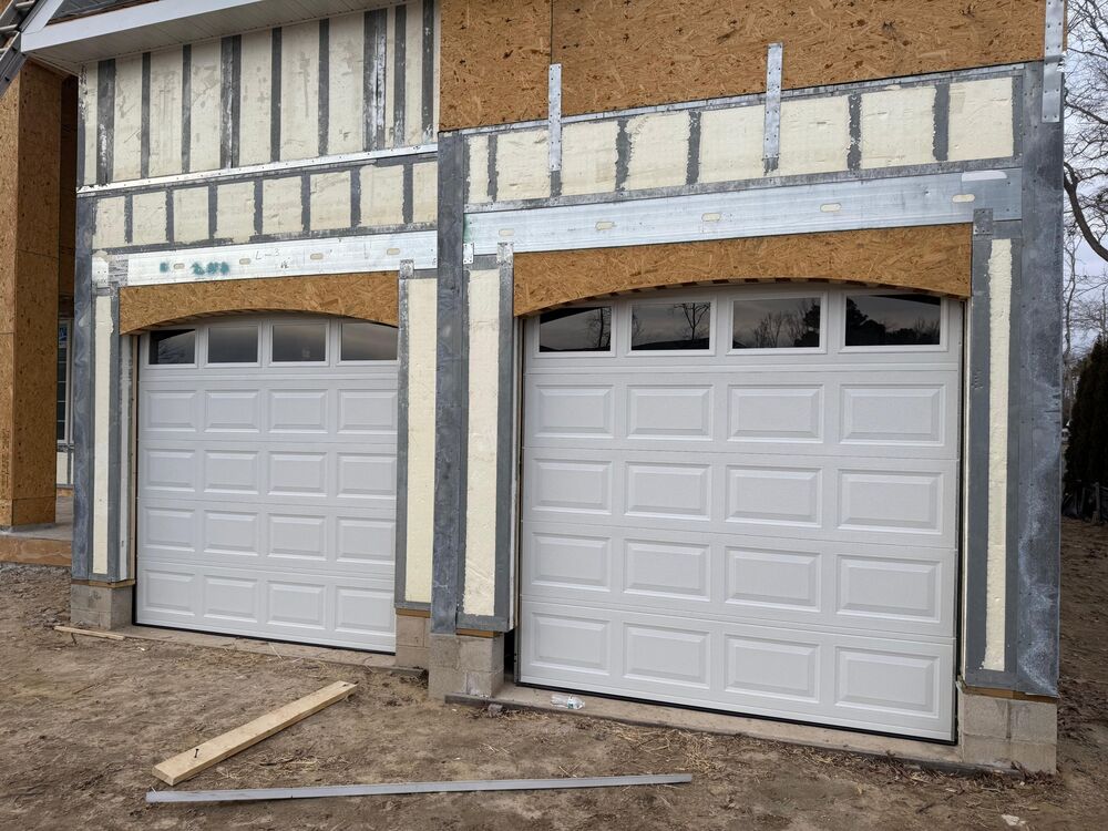 Two white raised-panel garage doors set into the openings of a new home under construction