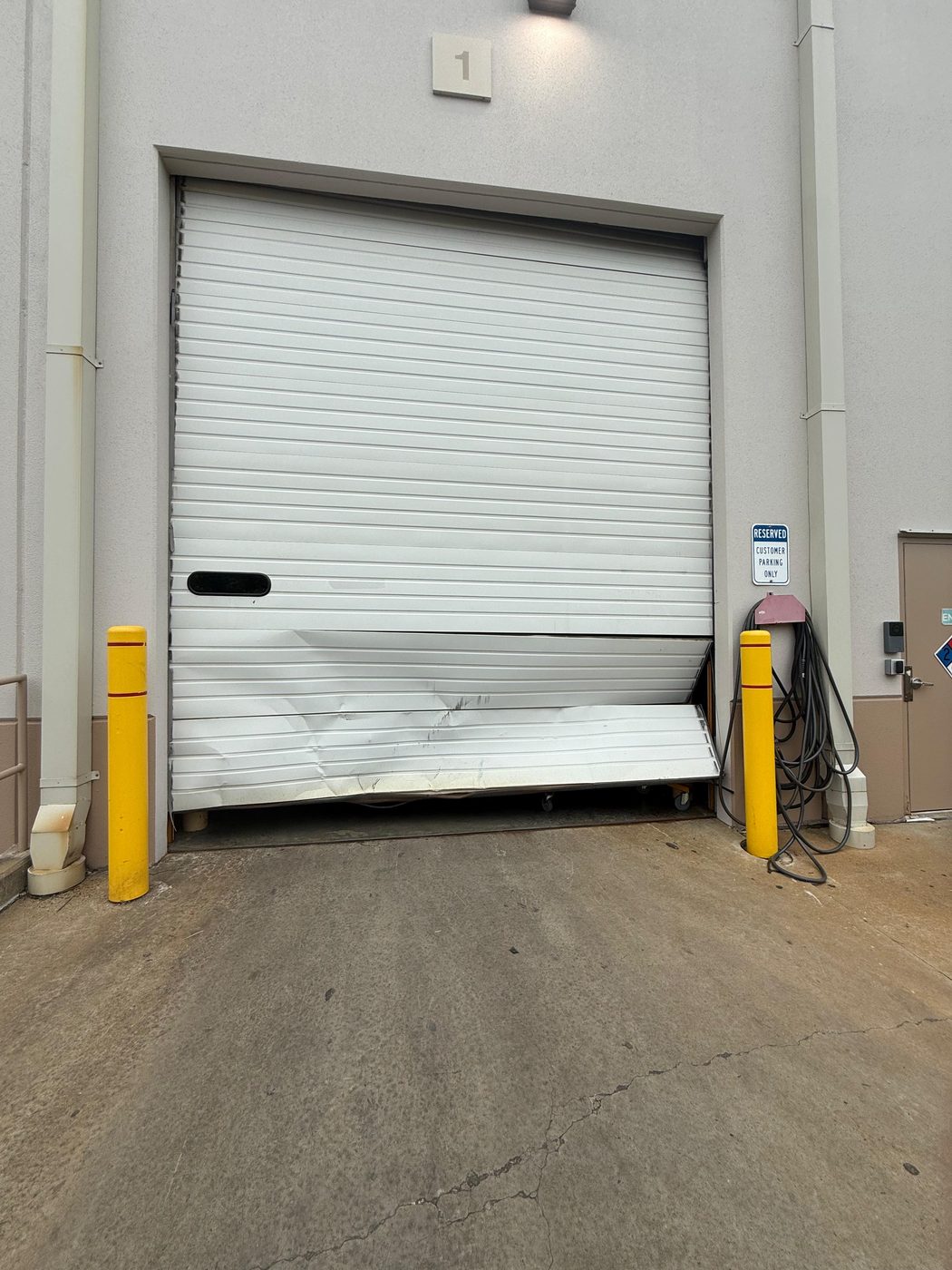 White commercial overhead door with dented, bent bottom panels between two yellow safety posts