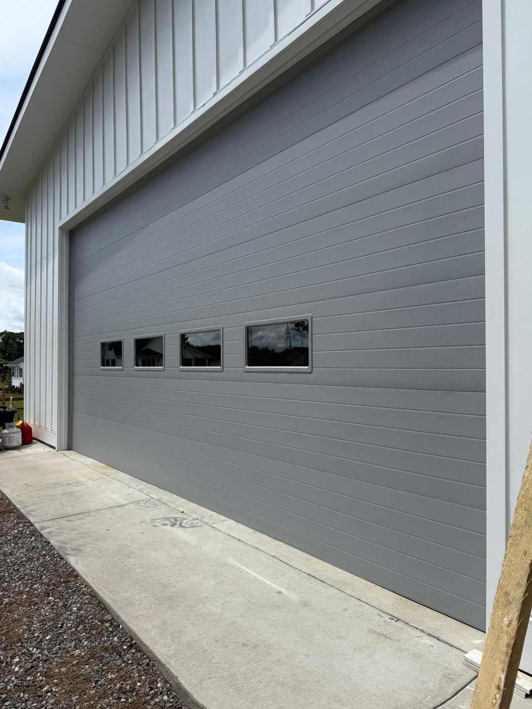 Gray garage door with a row of small windows on a white house