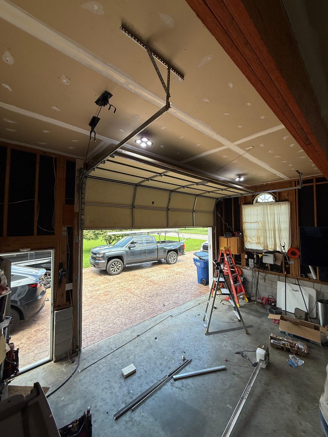 Inside a garage with the opener rail and door track being installed, with a ladder and parts on the floor